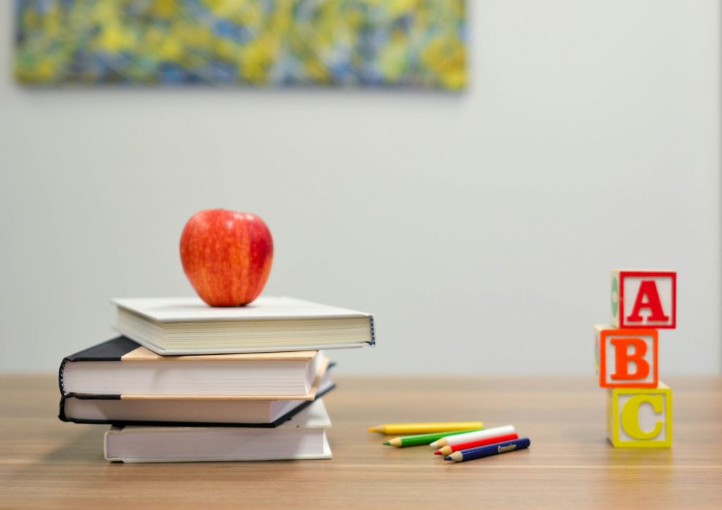 An apple on top of books. They are all on top of the table.