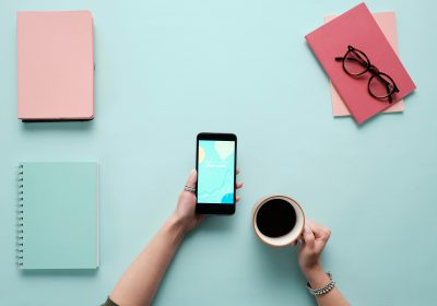 A woman holding a phone in the left hand side and a cup of coffee on the right hand side. Books all over the table.
